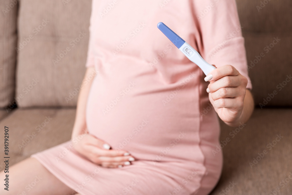 Young woman sitting on the sofa and show pregnancy test results Young woman sitting on the sofa and show pregnancy test results