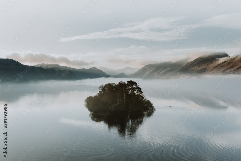 Misty morning on the lake with island reflections and low blue clouds. The Lake District, Cumbria. Autumn colours.  