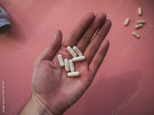 A hand with white pills and pink background. Medical concept