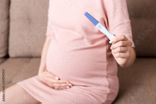 Young woman sitting on the sofa and show pregnancy test results