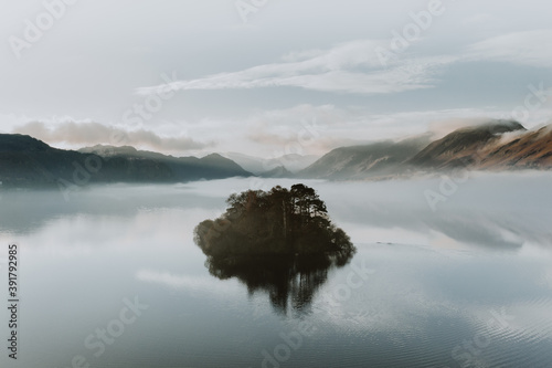 Misty morning on the lake with island reflections and low blue clouds. The Lake District, Cumbria. Autumn colours.  