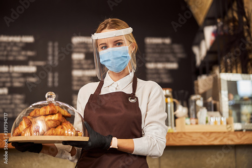Pretty waitress carrying tray of pastry in cafe during pandemic