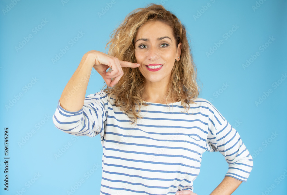 Fototapeta premium Young beautiful woman wearing casual clothes standing over blue isolated background smiling cheerful showing and pointing with fingers teeth and mouth. Dental health concept.