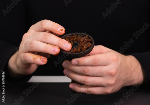 male hands put tobacco in hookah bowl on black background