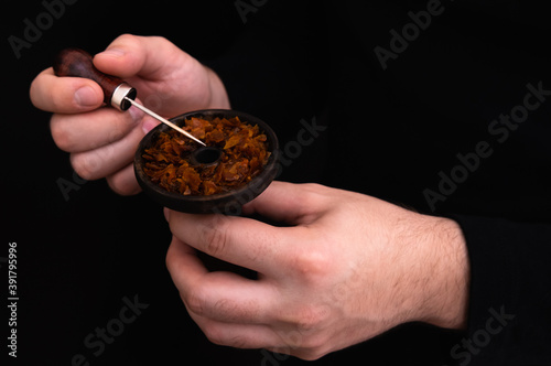male hands put tobacco in hookah bowl on black background