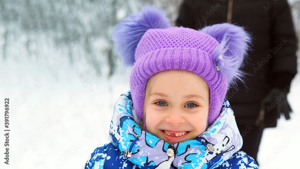 A little girl a child without front teeth walks in a winter hat during the snow season A little girl a child without front teeth walks in a winter hat during the snow season