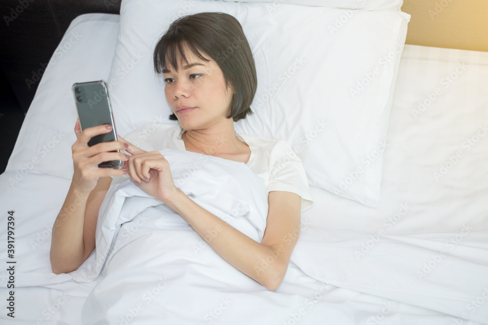 Young woman using smartphone mobile at white bed morning time Young woman using smartphone mobile at white bed morning time