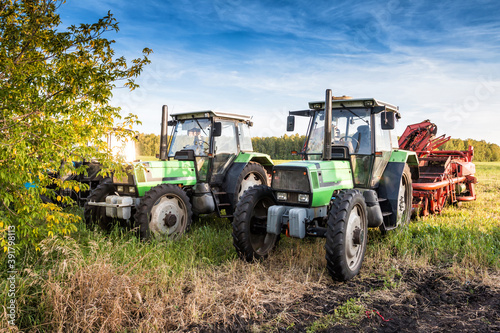 Modern wheeled agricultural tractors with harvesting equipment on an field