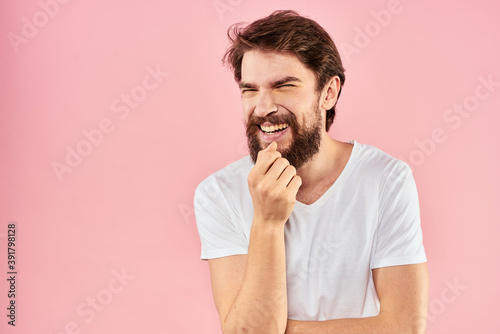 Bearded man in white t-shirt gesturing with hands facial expression close up pink background