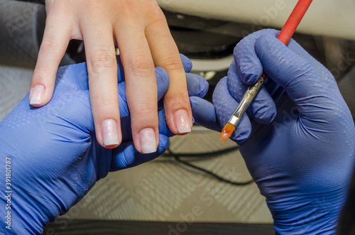 Close-up of beautician applies colored nail polish to a client in a salon. Nail care concept. Professional manicure.