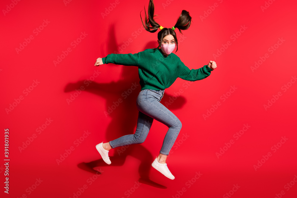 Profile side photo of pretty brown haired tails girl wear green sweater jeans mask run jump copyspace isolated on red color background