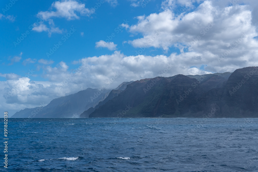 Hints of the Cathedrals of the Na Pali Coast can be seen at a distance poking through the coastline of the towering sea cliffs. The Cathedrals are a part of Honopū Valley.