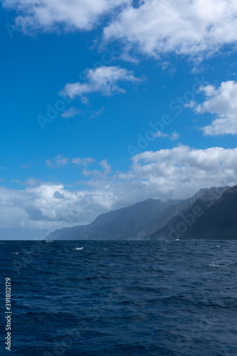 Hints of the Cathedrals of the Na Pali Coast can be seen at a distance poking through the coastline of the towering sea cliffs. The Cathedrals are a part of Honopū Valley. © Erin