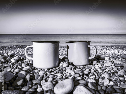Two travel mugs on the rocks in the beach with sea in the background. Monochrome filter. photo