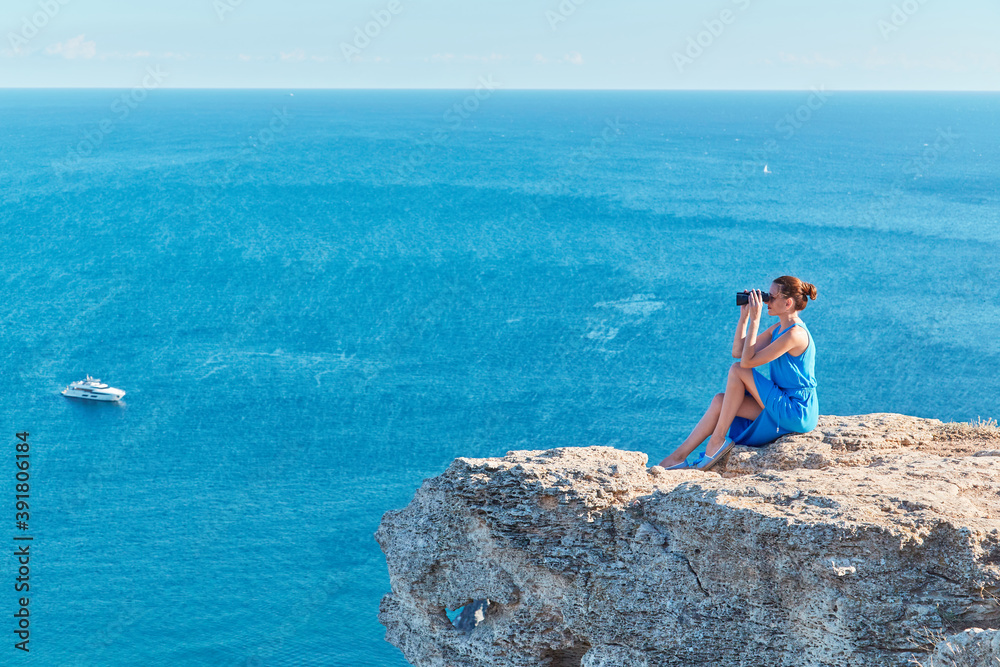 Beautiful sea view and woman sitting on mountain looking in binoculars. Travel time and new ground concept, copy space