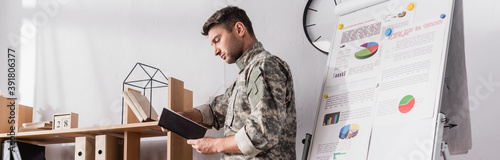 serious military man holding notepad near wooden rack and flipchart, banner