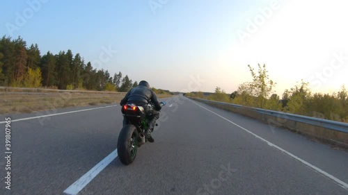 Follow to biker riding on modern sport motorbike on country road at sunset. Motorcyclist racing his motorcycle at highway. Guy driving bike during trip. Concept of journey and freedom. Aerial shot