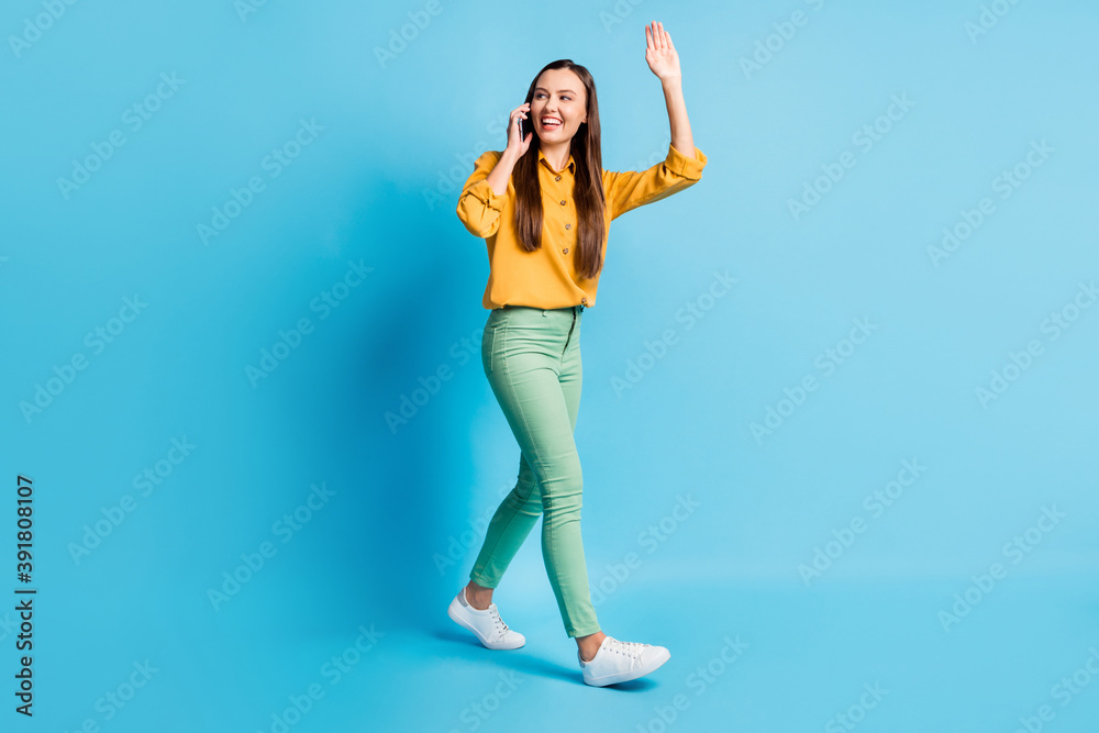 Full size profile photo of cute pretty lady talk telephone going waving hand wear shirt trousers sneakers isolated on teal background