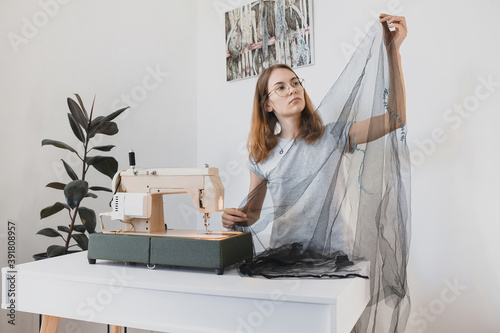 The girl Sewing dress made of black fabric tulle on a vintage sewing machine in the room workplace handmade photo