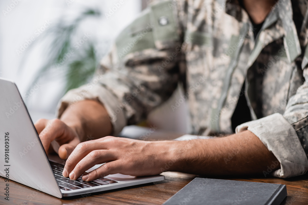 Cropped view of military man using laptop on desk - obrazy, fototapety, plakaty 