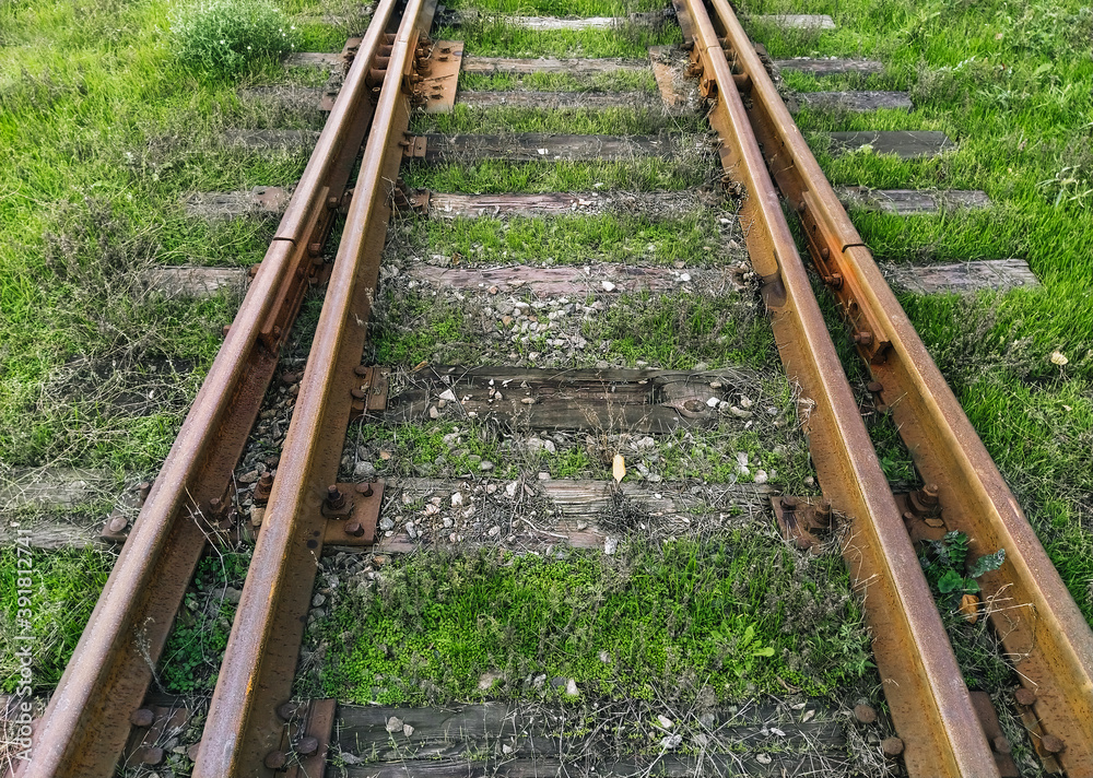 Old rusty, metal rails and wooden sleepers on a dirt surface with green grass. Railroad for passenger and freight trains. Photo, top view. Old rusty, metal rails and wooden sleepers on a dirt surface with green grass. Railroad for passenger and freight trains. Photo, top view.