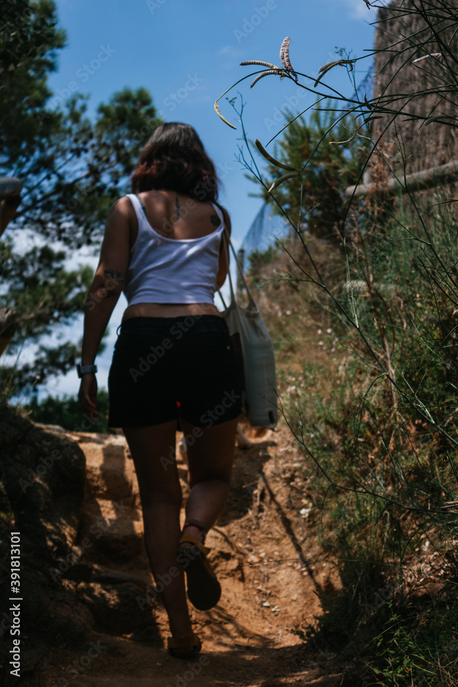Girl walking along a forest path during a mountain hike. Wears a white top and black short. Girl walking along a forest path during a mountain hike. Wears a white top and black short.