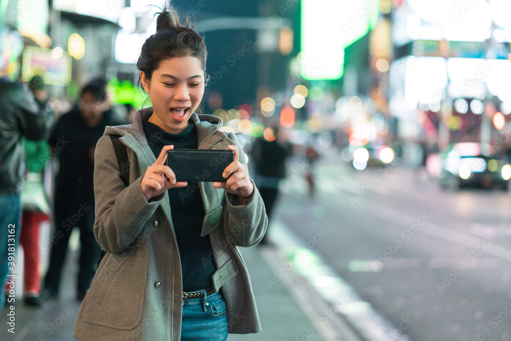 Fototapeta premium asian female traveller hand use smartphone and camera to capture photo in journey vacation night time nightlife in down town city street intersection light bokeh and crowd people tourists background