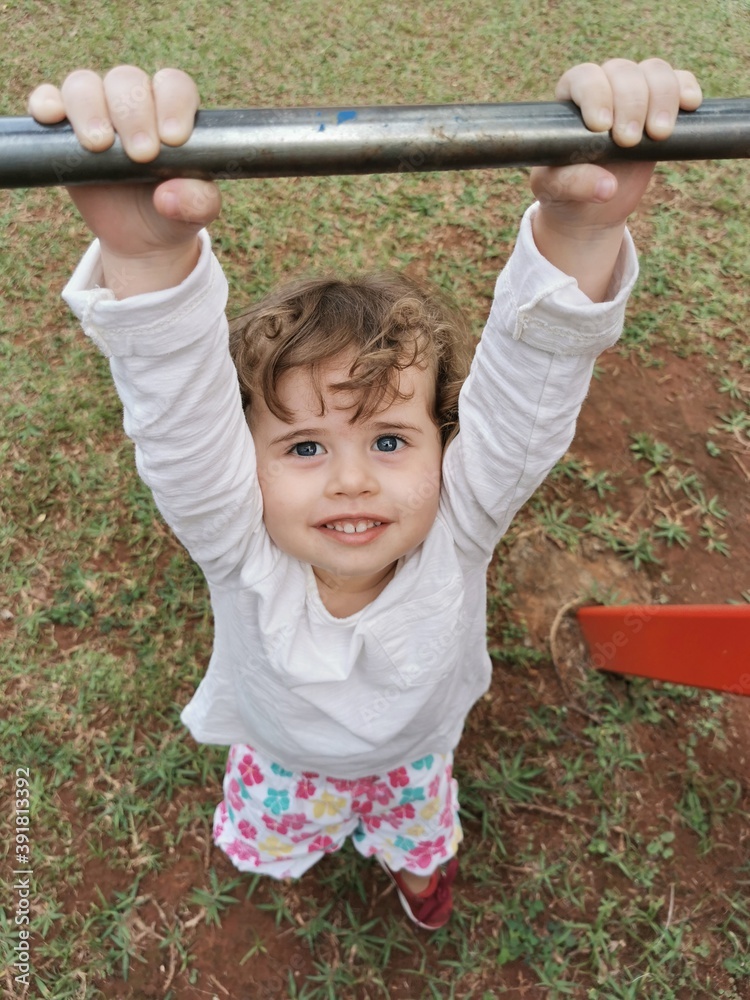 Portrait Brazilian Little girl playing hanging on bar at the playground Portrait Brazilian Little girl playing hanging on bar at the playground