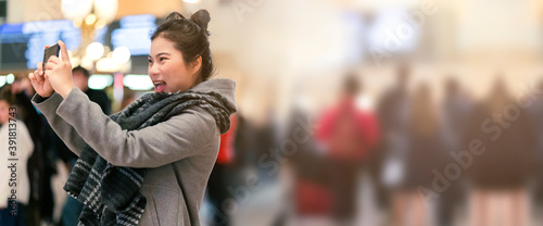 young asian female traveller sight seeing and enjoy advanture moment hand use smartphone take photo with background of grand central station and blur crowd people background