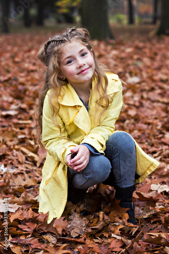 Little beautiful girl in a yellow raincoat walks in the park.