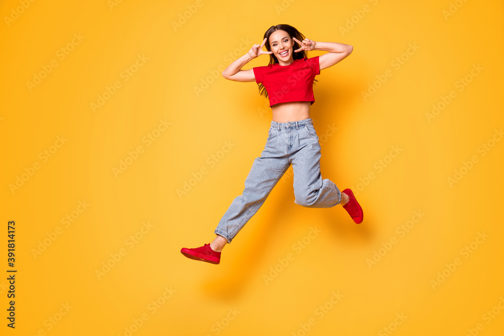 Full size photo of cute jumping lady showing v-sign symbols wear red crop top jeans shoes isolated yellow color background