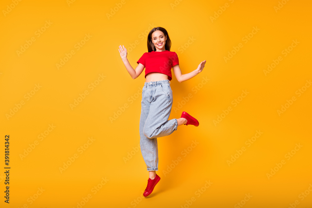 Full length photo of cute jumping lady wear red crop top jeans shoes isolated yellow color background