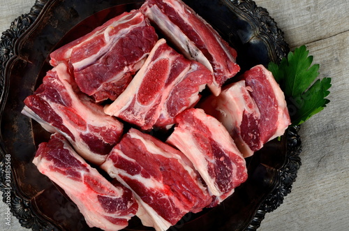 Raw meat ribs on a black silver plate, gray wooden background. Raw Organic Beef Short Ribs