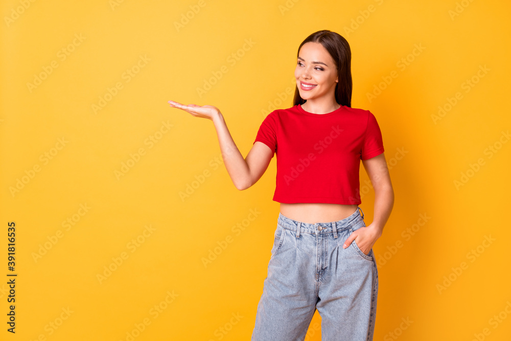 Attractive manager lady hold open palm presenting new object wear casual red top jeans isolated over yellow color background Attractive manager lady hold open palm presenting new object wear casual red top jeans isolated over yellow color background