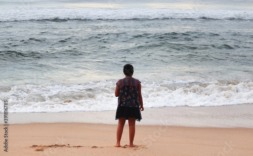 child walking on the beach. Indian girl on the sea shore watching the waves. Lonely girl at beach. Girl watching the sea.