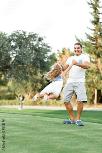 Father and daughter playing in meadow. Father holding daughter and spinning in circles, White and blue colors clothes
