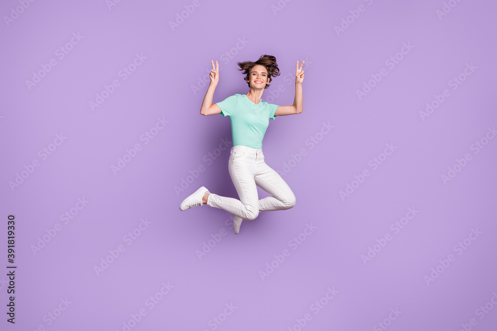 Full size profile photo of cute optimistic girl jumping show v-sign wear white sneakers pants blue t-shirt isolated on violet background Full size profile photo of cute optimistic girl jumping show v-sign wear white sneakers pants blue t-shirt isolated on violet background