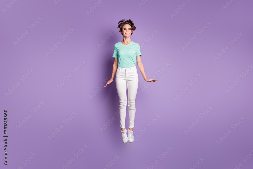 Full size photo of pretty cute girl jumping wear white sneakers pants blue t-shirt isolated on violet color background