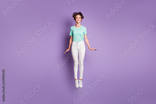 Full size photo of pretty cute girl jumping wear white sneakers pants blue t-shirt isolated on violet color background