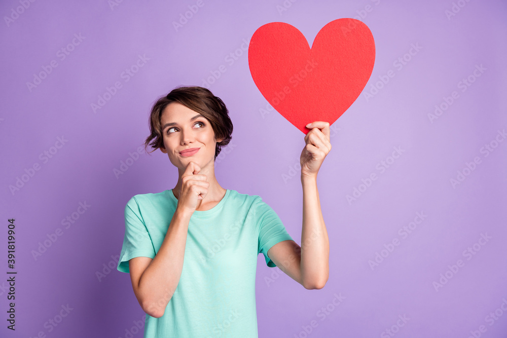 Photo of dreamy young lady wear casual teal outfit holding big red heart arm chin looking empty space isolated purple color background Photo of dreamy young lady wear casual teal outfit holding big red heart arm chin looking empty space isolated purple color background
