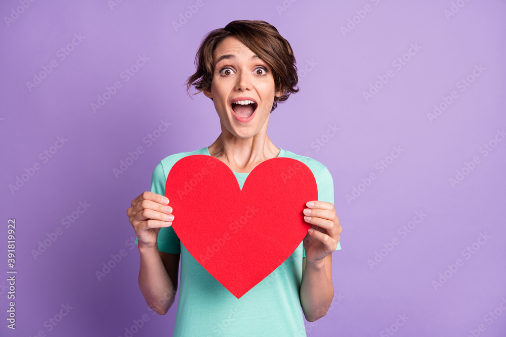 Photo of surprised young lady wear casual teal outfit holding big red heart isolated purple color background Photo of surprised young lady wear casual teal outfit holding big red heart isolated purple color background