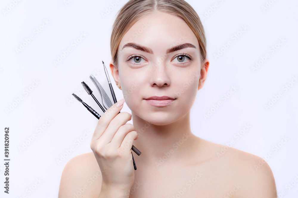 Young girl holding tools for correction and dyeing of eyebrows on a white background. Girl with beautiful eyebrows and skin. Long-term eyebrow styling and eyebrow lamination concept Young girl holding tools for correction and dyeing of eyebrows on a white background. Girl with beautiful eyebrows and skin. Long-term eyebrow styling and eyebrow lamination concept