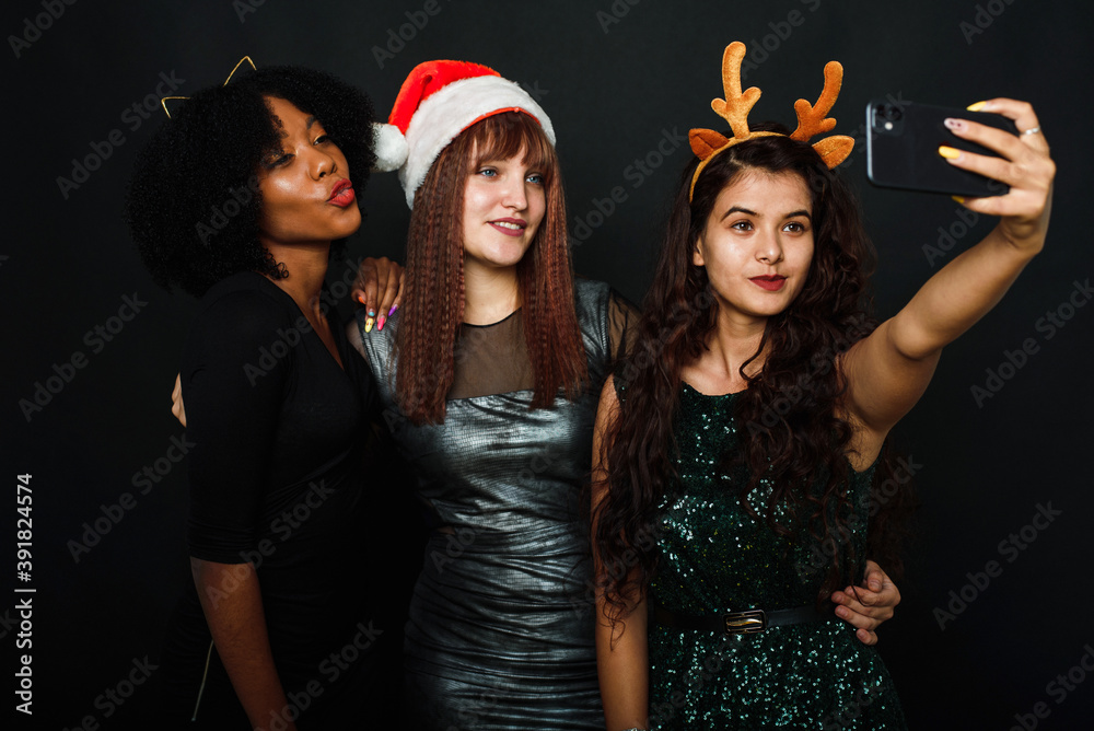 Group of friends at club making selfie and having fun. Cute young women posing with kissing face expression. Relaxed young women making selfie with friend on dark background during christmas Group of friends at club making selfie and having fun. Cute young women posing with kissing face expression. Relaxed young women making selfie with friend on dark background during christmas
