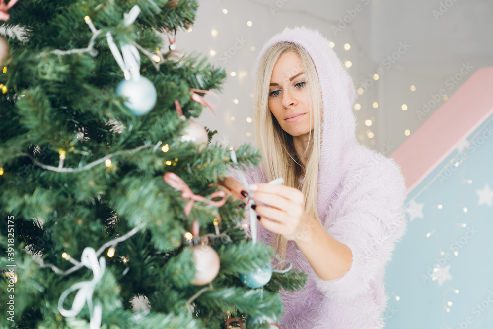 Pretty young woman with blond hair is decorating a Christmas tree
