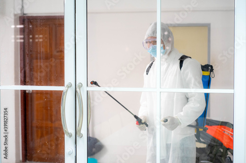 health care worker in white jumpsuit and protective face mask using spraying machine to disinfect virus pandemic.  Health care and midicine concept. New normal social distancing concept. © ake
