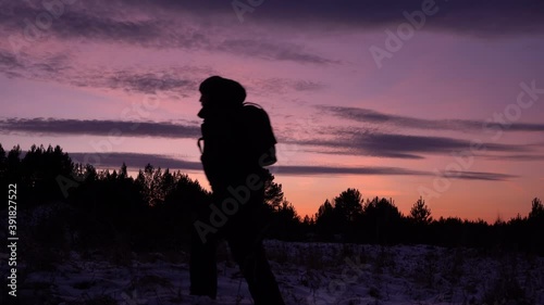 travel concept. black silhouette of a man in a hood against a purple sky. sunset in winter. travel in the winter forest photo