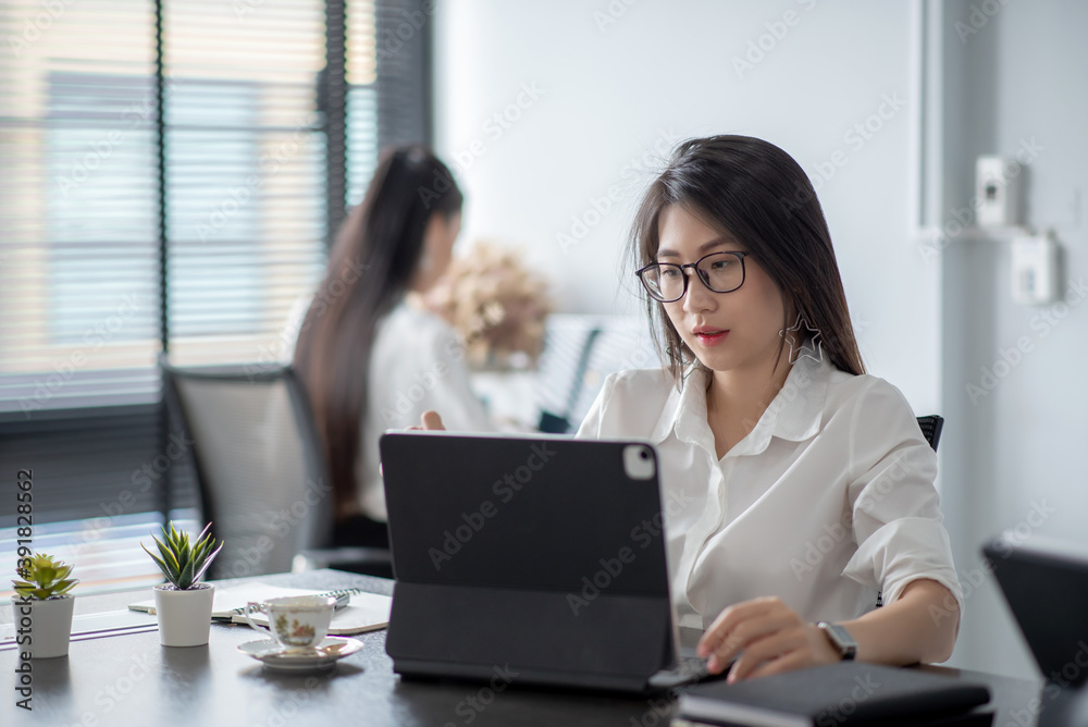 Pretty young asian woman working at desk with digital tablet in a modern office. Pretty young asian woman working at desk with digital tablet in a modern office.