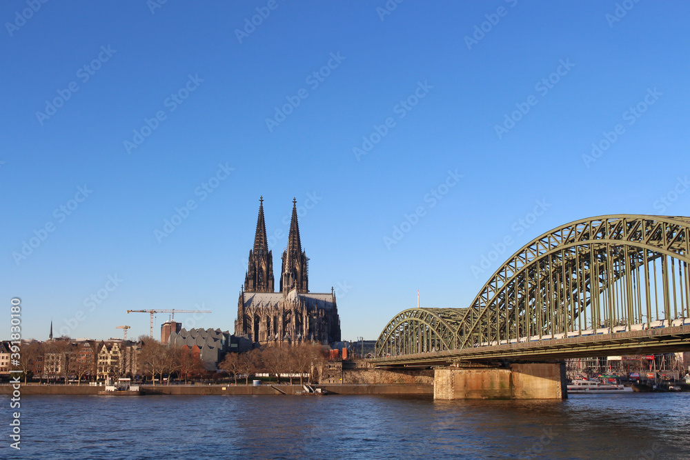 Naklejka premium The Hohenzollern bridge over Rhine river on a sunny day. The Cologne Cathedral (Kolner Dom) in the city of Cologne, Germany. It is the largest Gothic church in northern Europe.
