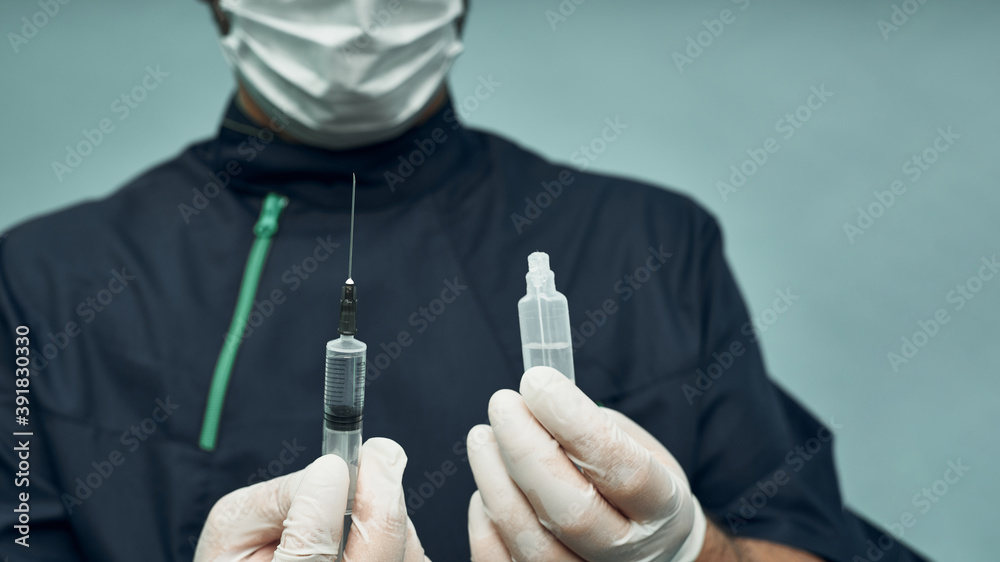 The doctor has a syringe and an ampoule in his hands. Professional clothing and mask with gloves. Vaccination. Coronavirus disease. The doctor has a syringe and an ampoule in his hands. Professional clothing and mask with gloves. Vaccination. Coronavirus disease.