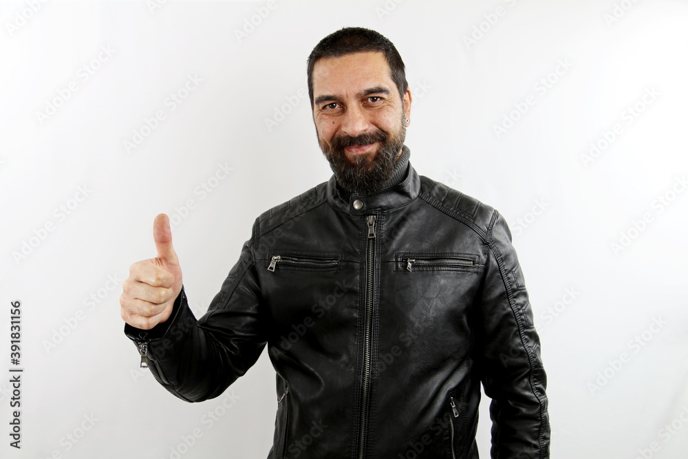 Young bearded smiling biker man with leather jacket on isolated white background making thumb up right sign.